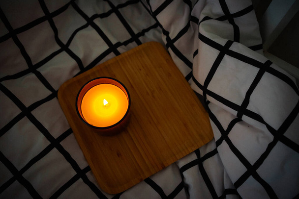 eco soy candle in a glass brown candle holder on a wooden tray in a black and white checkered bed. High quality photo - Foto, immagini