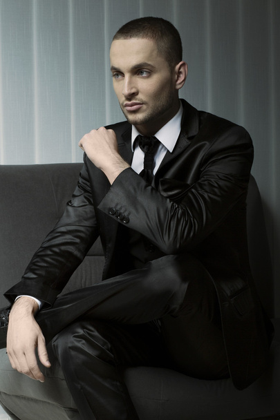 elegant young fashion man in tuxedo sitting on a sofa - Photo, Image