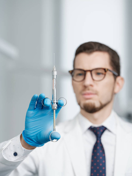 Closeup shot of syringe in hands of a male doctor. Doctor is blurred on a background. Selective focus - Photo, Image