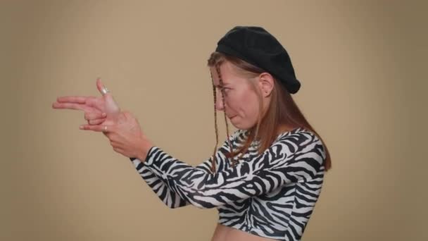 Pretty young woman pointing around with finger gun gesture, looking confident, making choice, shooting killing with hand pistol right on target. Adult stylish girl isolated on beige studio background - Záběry, video