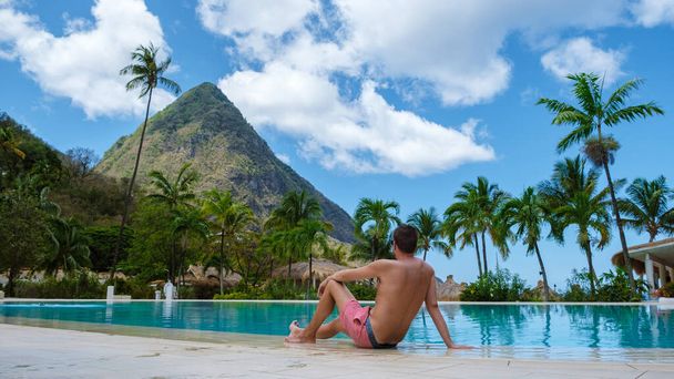 Sugar beach Saint Lucia is a public white tropical beach with palm trees and luxury beach chairs on the beach of the Island St Lucia Caribbean. young men in a swim short at the edge of an infinity - Foto, Imagem