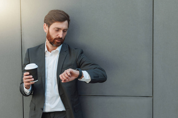 Focused businessman in suit with coffee watching on his wrist watch during break. Business concept - Photo, Image
