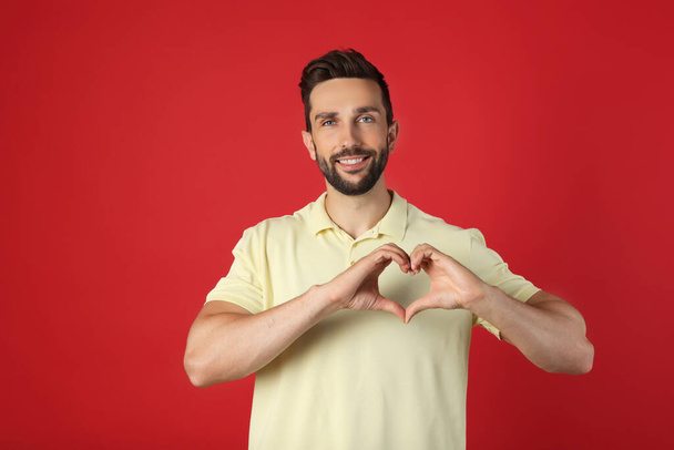Happy man making heart with hands on red background - Foto, afbeelding