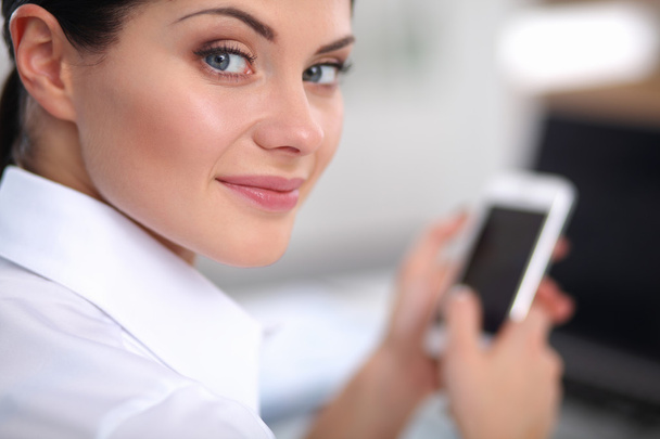 Businesswoman sending message with smartphone sitting in the office - Fotó, kép