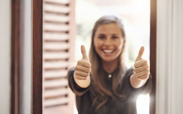 Thumbs up from a happy woman smiling while showing a hand winning gesture in a modern office. Cheerful, positive female looking excited after getting good news, feedback or a promotion at work. - Foto, Imagem