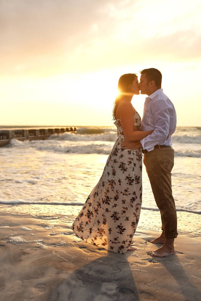 Moments like these. Full length shot of an affectionate young couple kissing while standing on the beach - Photo, Image