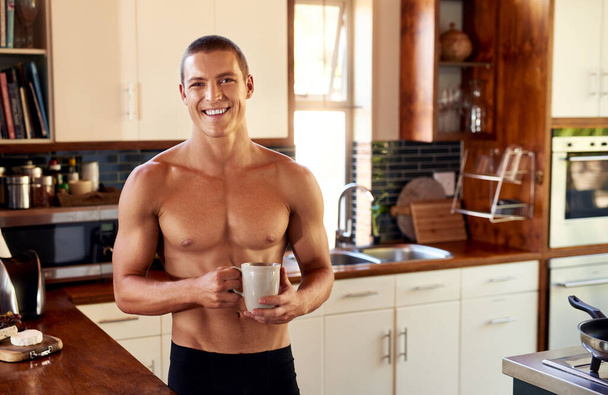 To cheer up he has a cup of coffee. handsome young shirtless man drinking a cup of coffee in the kitchen at home - Fotó, kép
