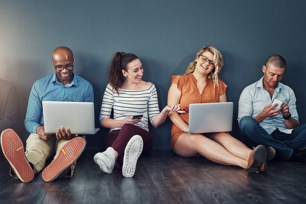Diverse modern group of business people sitting on social media networking apps on their digital devices. creative team of work colleagues connected online with laptop pcs and phones. - Foto, Imagem