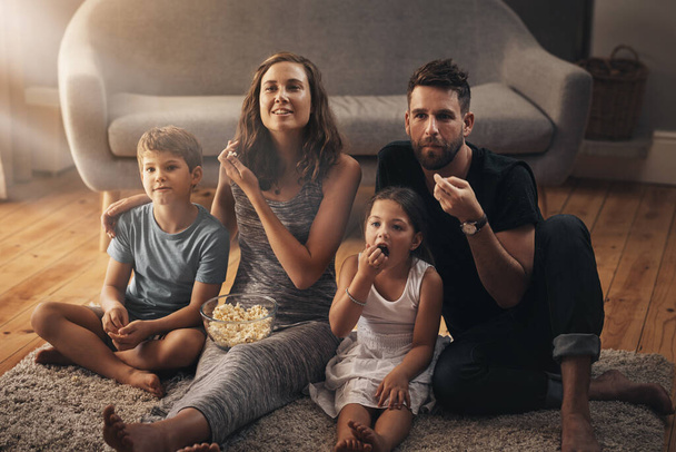Turning their living room into a cinema. a young family relaxing on the floor and watching movies together at home - Photo, Image