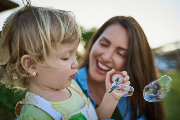 Ill blow and you catch them Mommy. a mother and her little daughter blowing bubbles outdoors - Foto, afbeelding