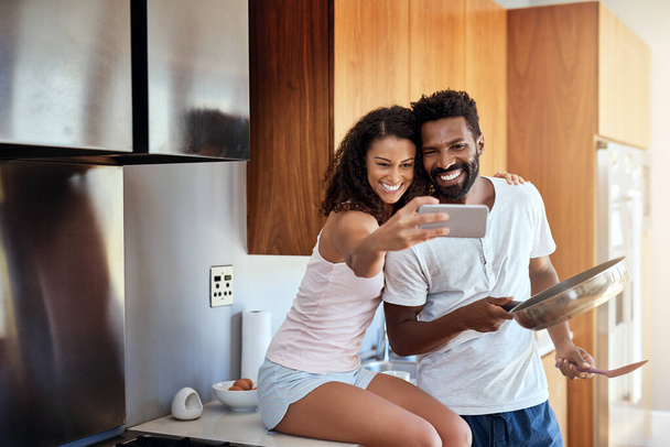 Selfies in the kitchen. an attractive young woman taking selfies of herself and her husband while he cooks in the kitchen - Foto, imagen