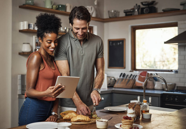 Young couple cooking healthy food together following recipes online on a tablet, step by step. Happy, cheerful and smiling husband and wife making dinner in the kitchen at home - Foto, Imagem