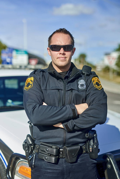 Я на работе. Обрезанный портрет красивого молодого полицейского, стоящего со скрещенными руками во время патрулирования - Фото, изображение
