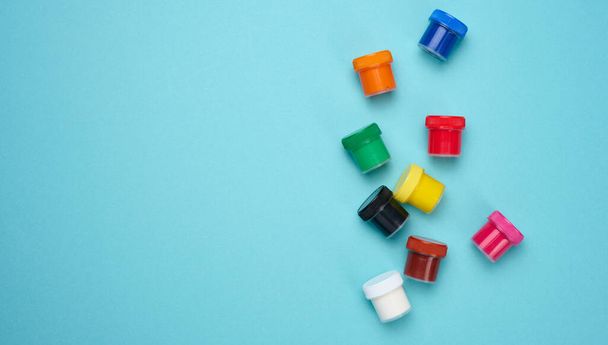 Plastic jars with multi-colored gouache on a blue background, copy space - 写真・画像