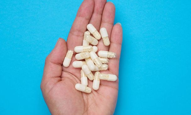 Woman's hand holding white oval pills on blue background, close up - Foto, afbeelding
