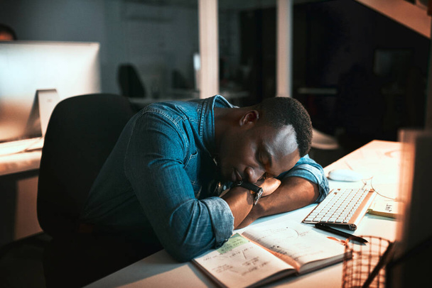 Totally exhausted. High angle shot of a young male designer sleeping at his desk while working late in the office - 写真・画像