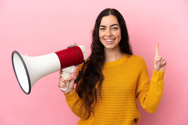 Young caucasian woman isolated on pink background holding a megaphone and pointing up a great idea - Photo, image