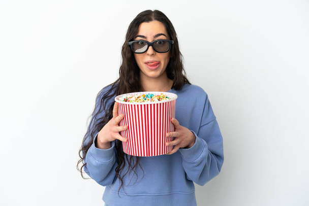 Young caucasian woman isolated on white background with 3d glasses and holding a big bucket of popcorns - Фото, изображение