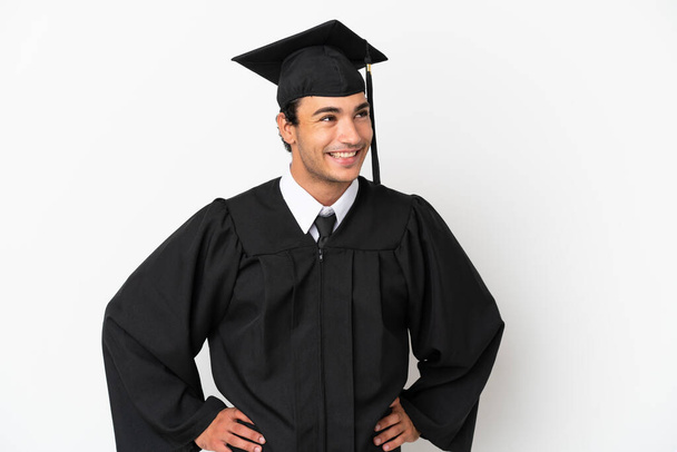 Joven graduado universitario sobre fondo blanco aislado posando con los brazos en la cadera y sonriendo - Foto, imagen