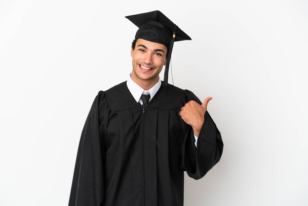 Молодой выпускник университета на изолированном белом фоне, указывая на сторону, чтобы представить продукт - Фото, изображение