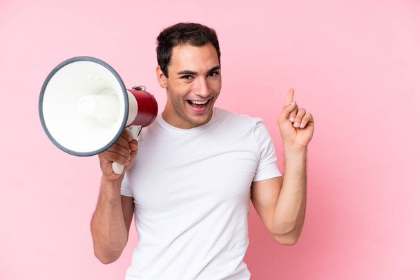 Young caucasian man isolated on pink background shouting through a megaphone and pointing side - Photo, Image