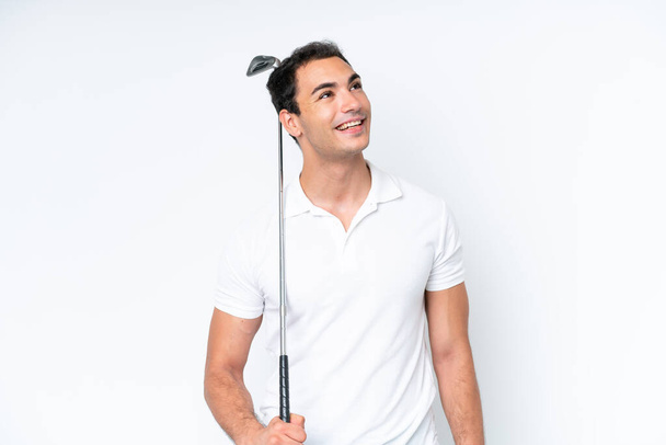 Молодой кавказский человек изолирован на белом фоне играет в гольф и смотрит вверх, улыбаясь - Фото, изображение