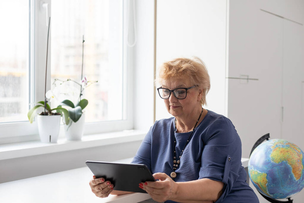 Ηλικιωμένη γυναίκα που χρησιμοποιεί ψηφιακή πλακέτα στο σπίτι. Η χρήση της τεχνολογίας από τους ηλικιωμένους. - Φωτογραφία, εικόνα