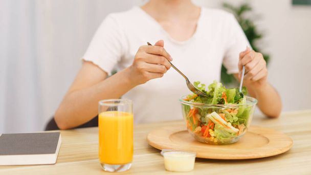 Lifestyle in living room concept, Young Asian woman mixing vegetable salad in bowl for breakfast. - Photo, Image
