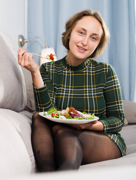 Young woman sitting on sofa at home and eating healthy food - Фото, зображення