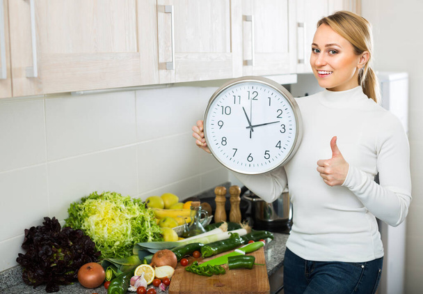 Young blonde woman cooking vegetables and looking at clock at home kitchen. - Foto, immagini