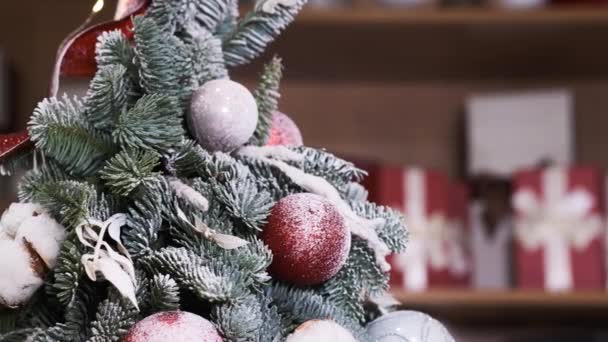 Вращающаяся елка с красными игрушками, шарами, снегом на фоне размытых подарочных коробок. Новогодняя композиция. - Кадры, видео