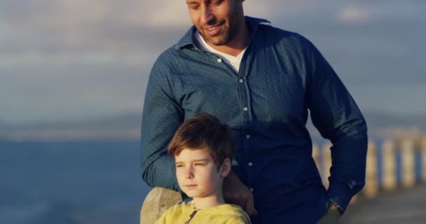Father and son bonding and spending time together while admiring the calm ocean. Little boy pointing and showing view while standing with his single dad on a seaside promenade on overcast family day. - Кадри, відео