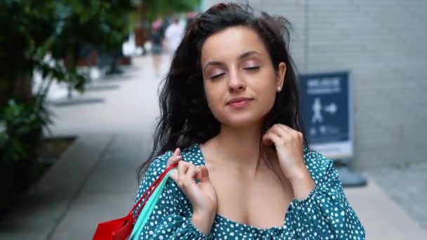 Close up of young Caucasian brunette woman walking outdoors with bags after shopping in good mood and touching her hair. Beautiful female buyer with purchases and packets on street. Buying concept - Video, Çekim