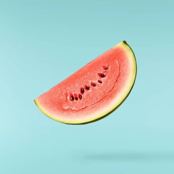 Fresh raw watermelon falling in the air isolated on blue background. Food levitation or zero gravity conception. igh resolution image. - Photo, Image
