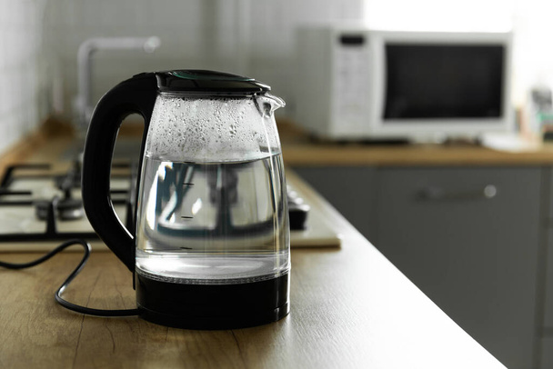 Modern electric transparent kettle on a wooden table in the kitchen.Kettle for boiling water and making tea.Home appliances for making hot drinks.Space for copy.Place for text. - Foto, afbeelding