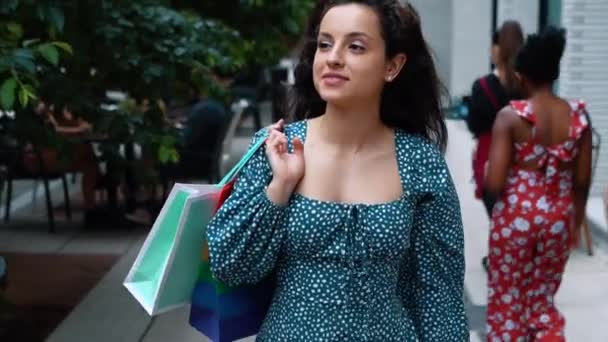 Close up portrait of joyful contented Caucasian female in dress walking in good mood after shopping in city. Positive young woman with bags goes from shopping mall. Happy emotions. Slow motion - 映像、動画