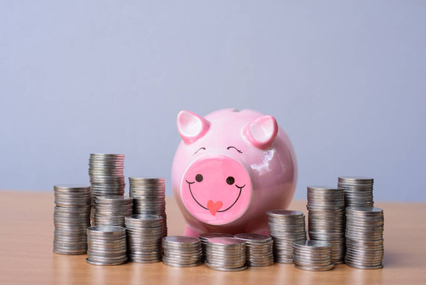 Close up of happy piggybank and coin towers on wooden table. - Foto, imagen