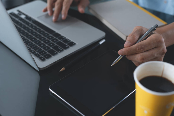 Случайный деловой человек, дизайнер, фрилансер ручка во время работы на ноутбуке с цифровым планшетом и чашкой кофе на столе в офисе, стартап бизнес и современная концепция технологии - Фото, изображение