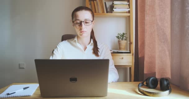 Young woman yawns while sitting workplace, laptop, desktop, looks out window. Front view, portrait. Concept of work fatigue, overwork, boring work, home office, learning, freelancing, student. High - Video