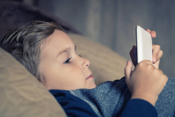Дитина лежить у ліжку і дивиться мультфільми на цифровому планшеті. Маленький хлопчик використовує тачпад і читає історію ввечері
. - Фото, зображення
