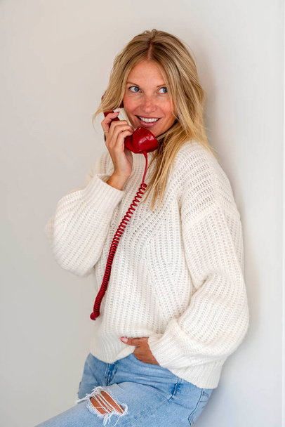 Шикарная блондинка-модель разговаривает по телефону, демонстрируя эмоции в домашней обстановке - Фото, изображение