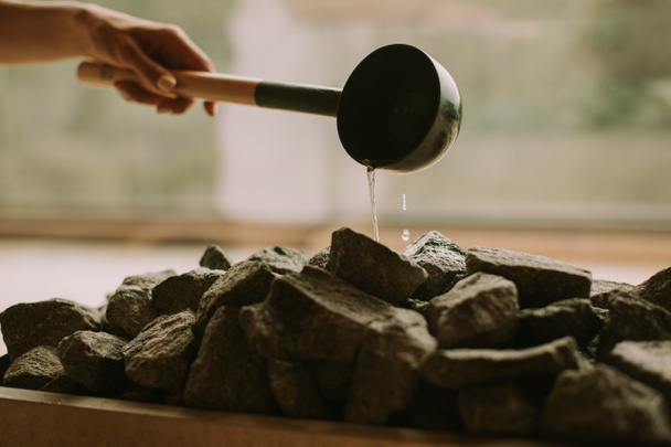 Young woman hand pouring water on hot rocks in the sauna - Foto, Imagen
