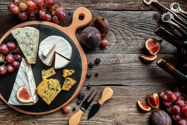 Különféle sajtok, hagyományos francia, olasz és spanyol manchego sajtok szőlővel és fügével, fából készült asztalon tálalva. - Fotó, kép