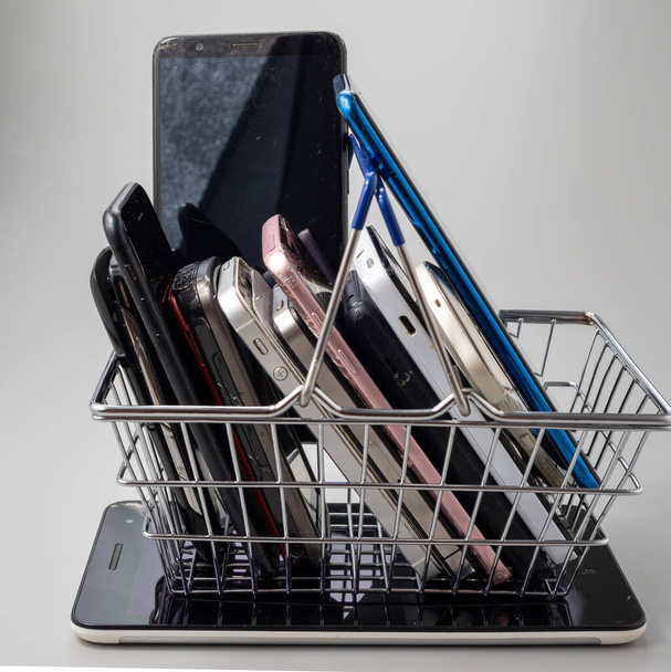 Phones of different models and generations are in the shopping cart. Smartphones on a gray background. - Foto, Imagen