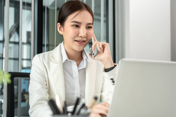 Asian businesswoman talking on the phone and use the laptop to work with a colleague in a private office, Telephone communication, Emote conversation, World of communication technology - Foto, Bild