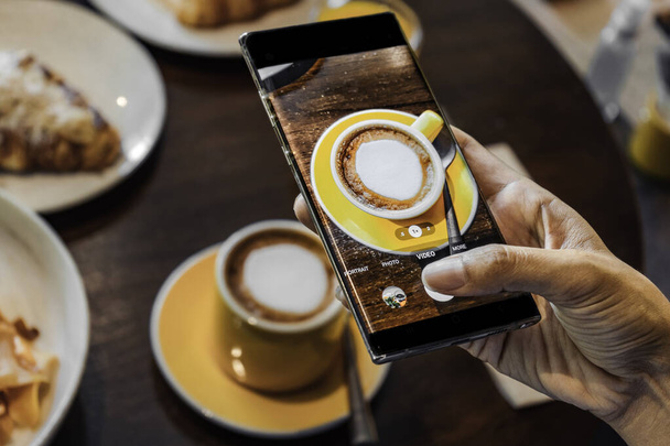 Рука женщины фотографирует чашку кофе с помощью мобильного телефона. Высокое качество фото - Фото, изображение