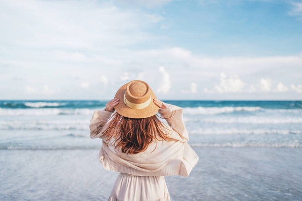 Summer beach vacation concept, Young woman with hat relaxing with her arms raised to her head enjoying looking view of beach ocean on hot summer day, copy space. - Fotoğraf, Görsel