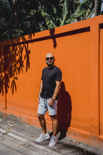 Male model with beard wearing black blank t-shirt on the background of an orange wall. - Photo, Image