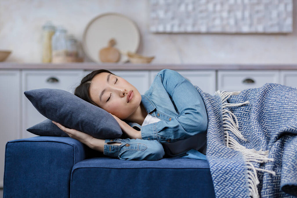 Close-up photo of a young beautiful Asian woman sleeping at home lying on the sofa covered with a blanket, resting after work for in the living room woman with closed eyes - Foto, immagini