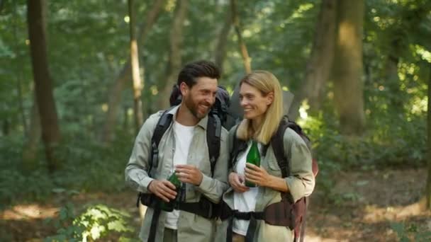 Couple leisure. Happy middle aged man and woman backpackers walking in forest, drinking water and talking, enjoying nature, tracking shot, slow motion - Metraje, vídeo